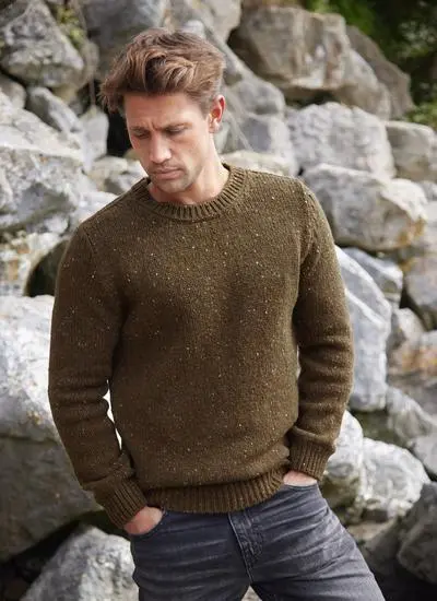 Man on a beach wearing an olive flecked fisherman crew neck sweater