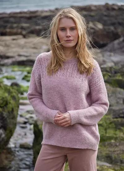 blonde woman standing in rocky beach wearing a pink eyelet crew knit sweater