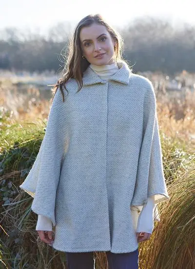 Woman standing against wintery countryside backdrop wearing cream wool cape. 