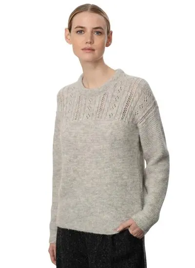 woman in studio wearing an off-white eyelet stitch woolen sweater with one hand in pocket
