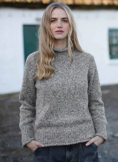 blonde woman standing in front of cottage wearing grey sweater