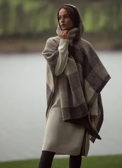 Woman standing in front of lake wearing silk slip dress and beige check cape with hood up.