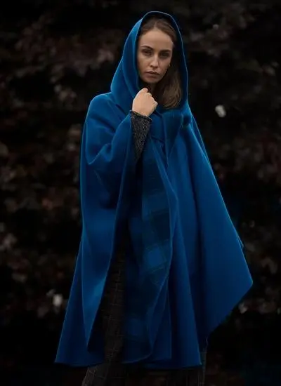 Woman standing outside wearing blue cape with hood.