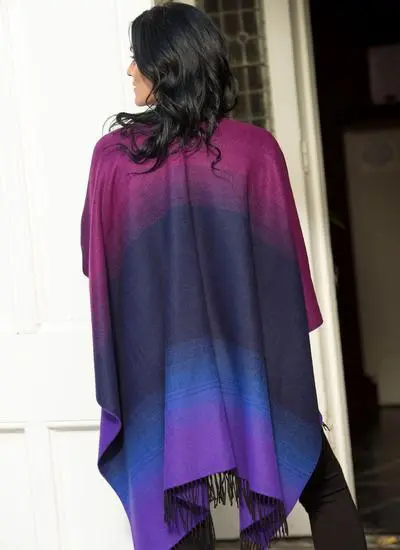 Back angle shot of brunette woman wearing purple and black shawl standing in front of building. 