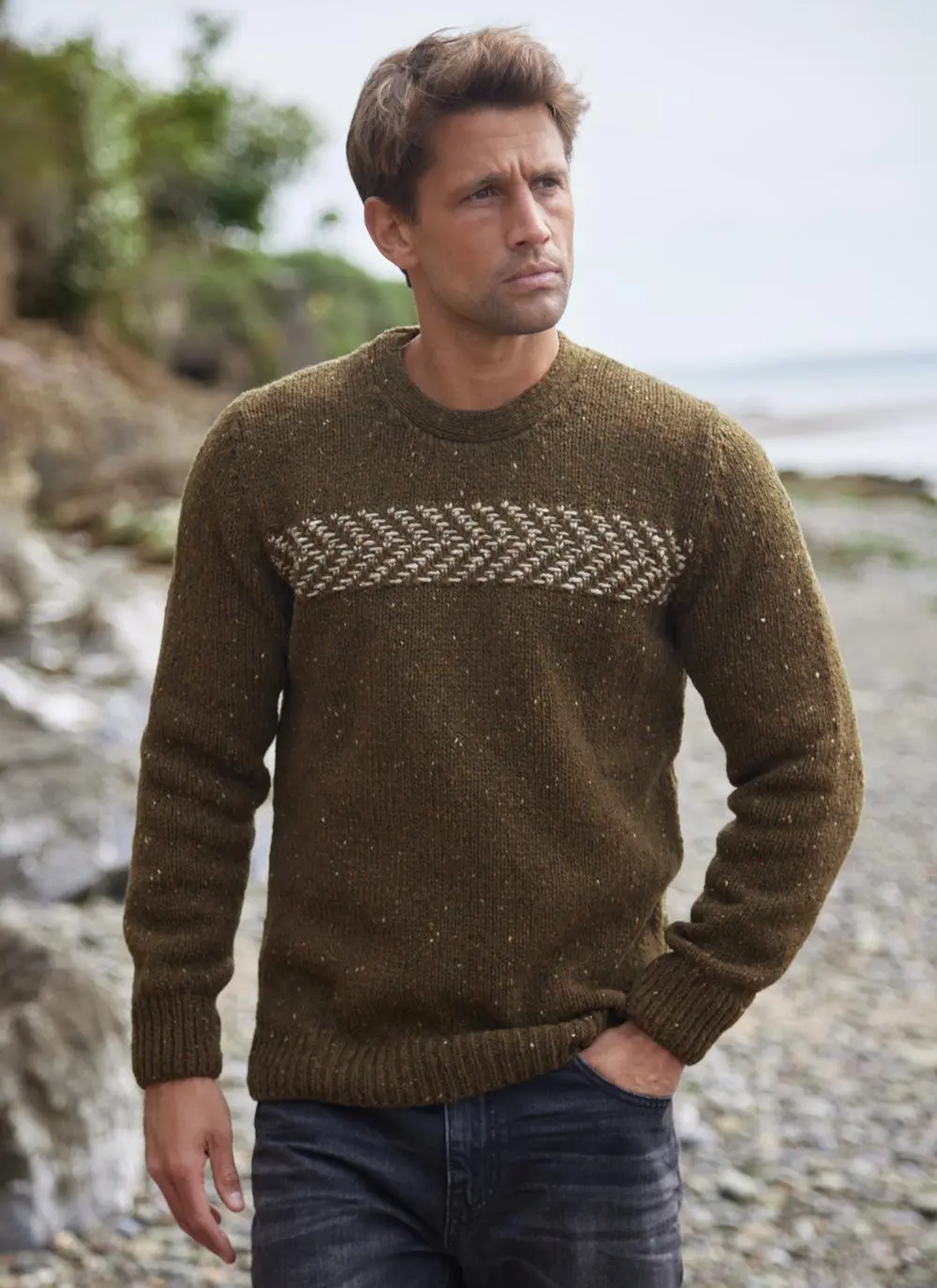 Man on beach wearing two tone crew neck sweater, hand in pockets