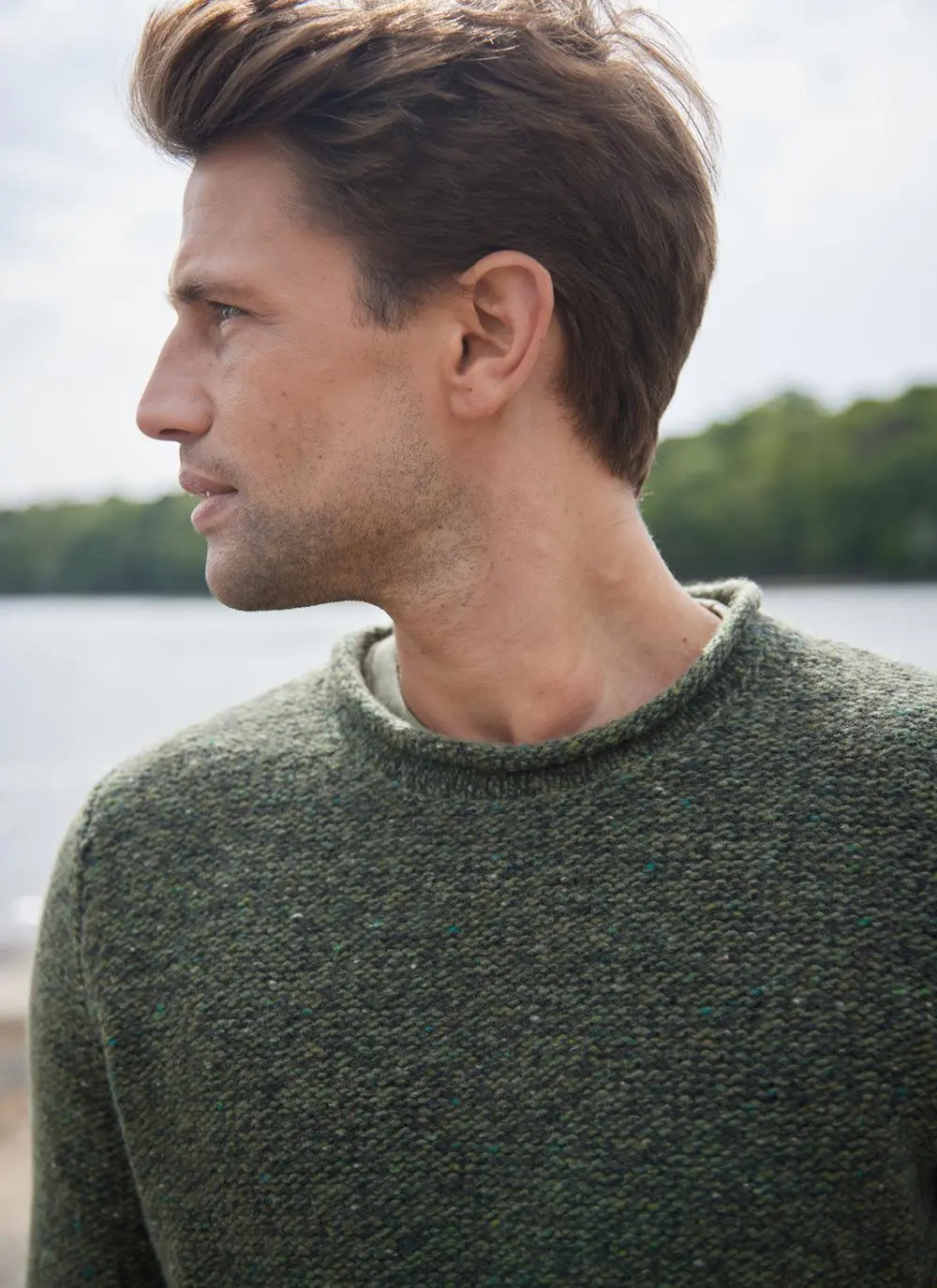 Man on beach wearing an olive green fisherman sweater with rolled neck and sleeves, close up