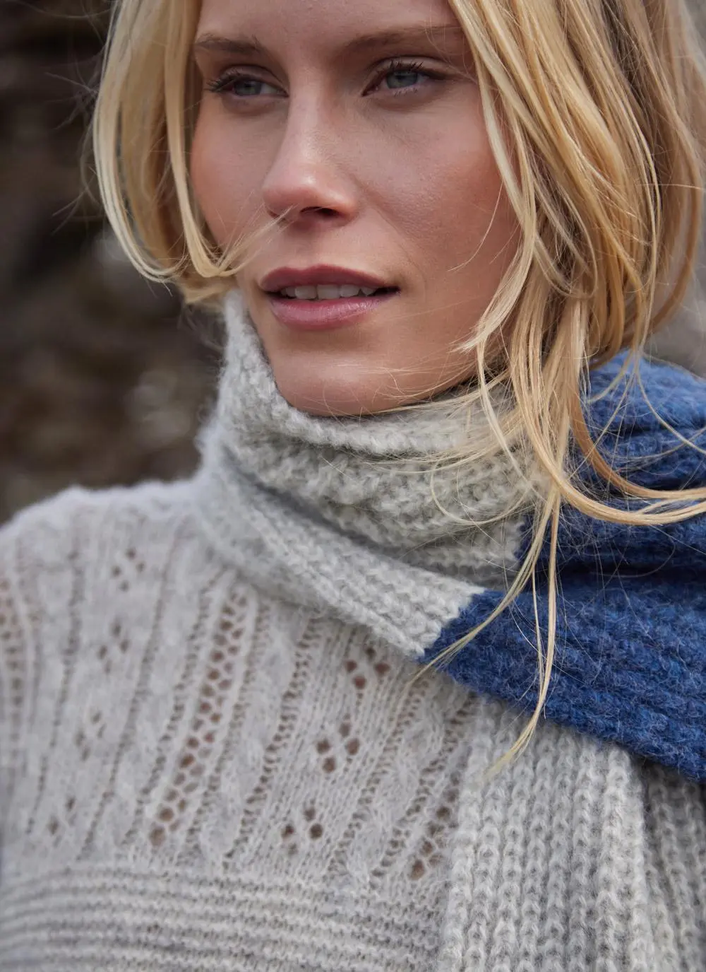 close up of blonde woman wearing a large grey and blue knit scarf 