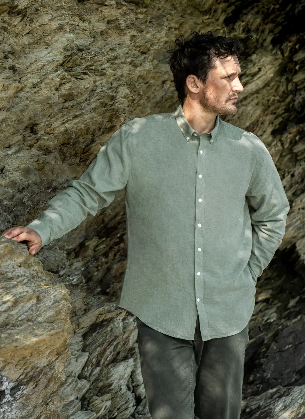 Model standing against a rock face in Finn Cotton Linen Shirt in Green, hands in pockets – casual yet refined men’s look.