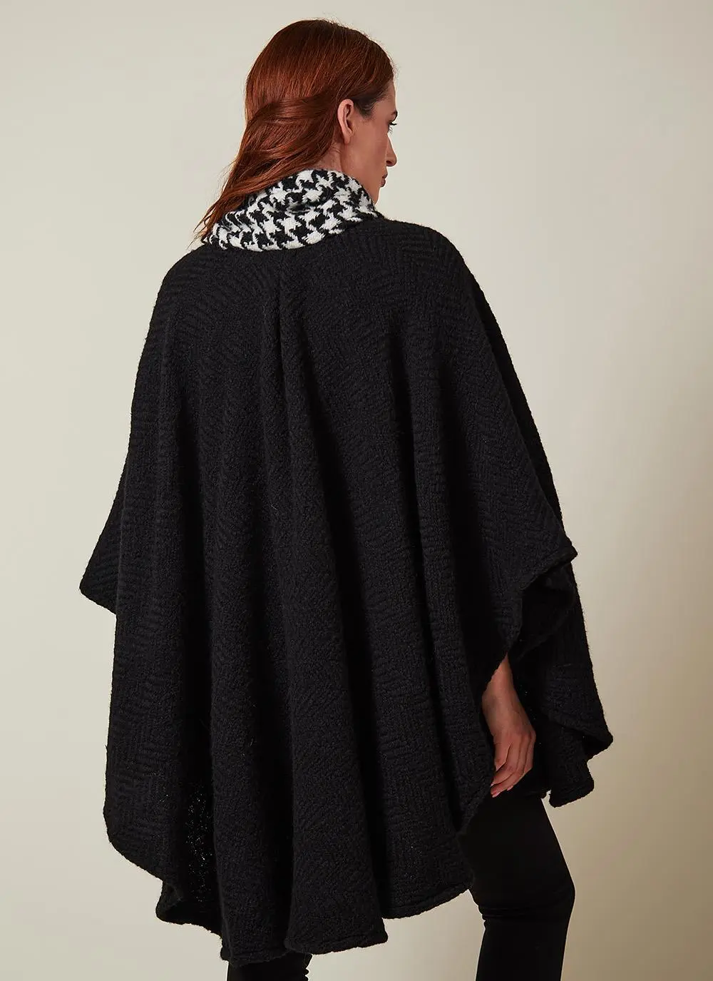 Studio back angle shot of auburn haired woman wearing black wool cape with houndstooth scarf.