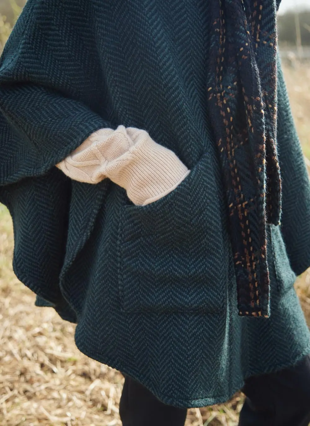 Pocket of woman in grassy Irish countryside wearing dark green herringbone cape.