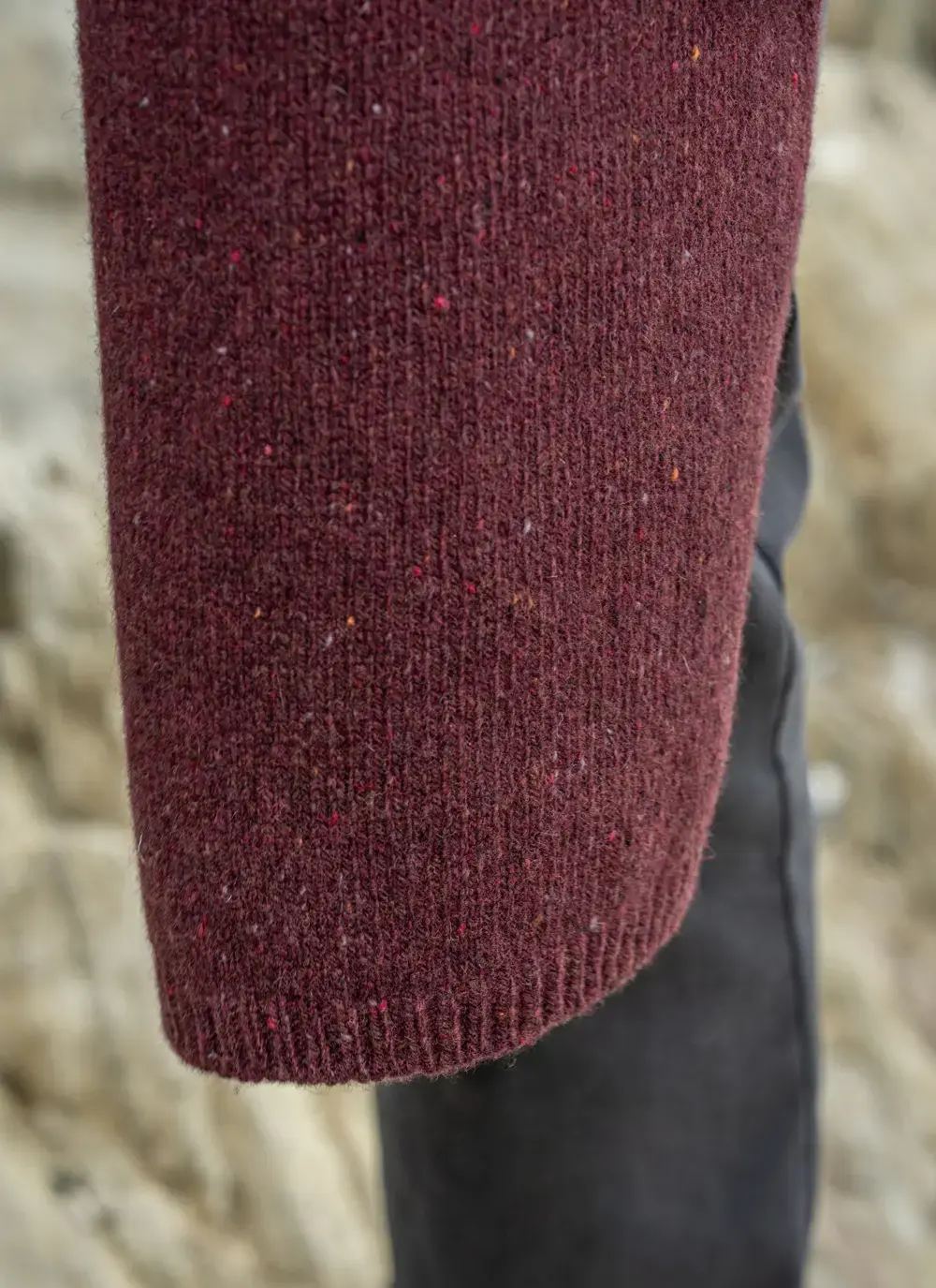 Man wearing a burgundy wool cashmere tweed scarf draped over a green sweater, standing on a rocky coastal path in Ireland.