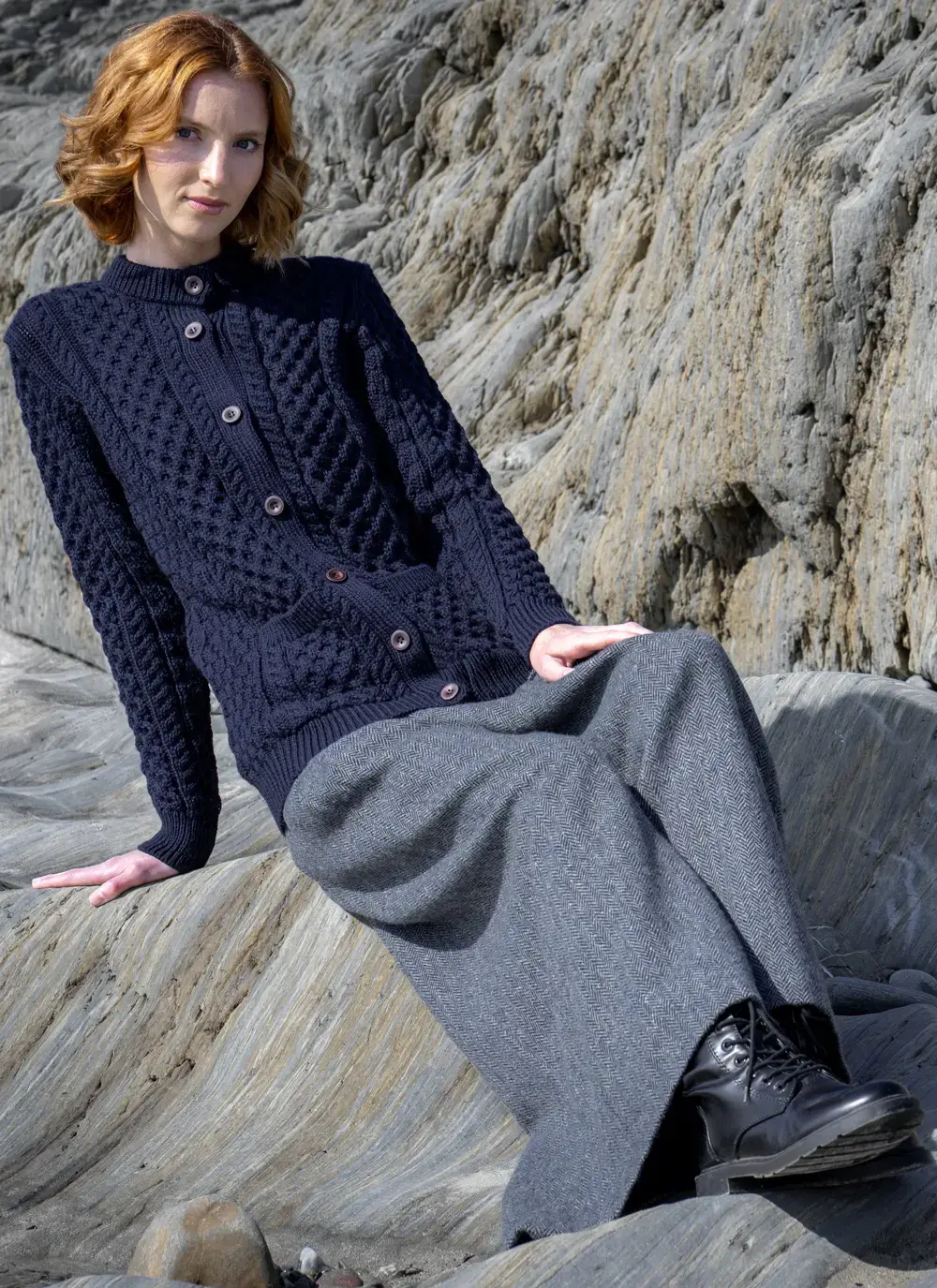 red head model sitting on rock in dark navy mary lumber aran cardigan