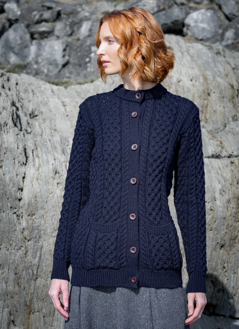red head model standing on rock looking away in dark navy mary lumber aran cardigan