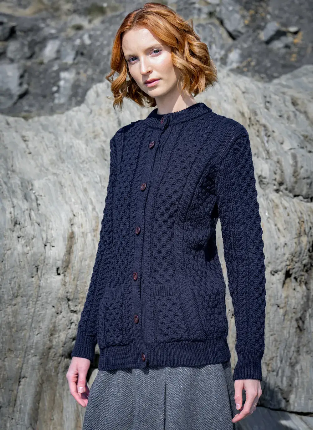 red head model standing on rock looking forward in dark navy mary lumber aran cardigan