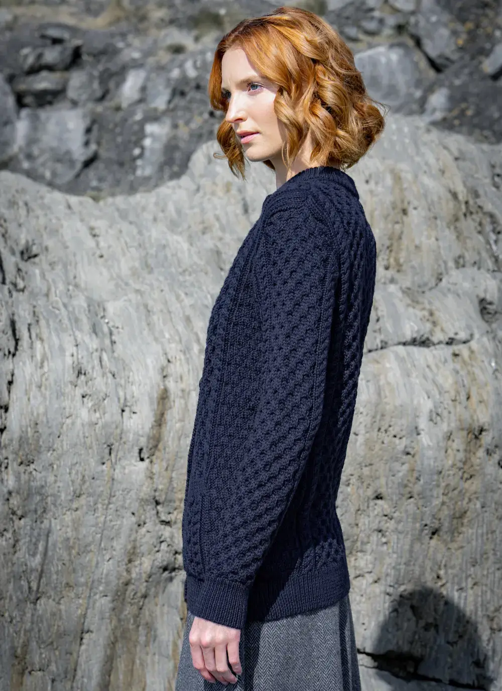 red head model standing on rock looking away side ways in dark navy mary lumber aran cardigan