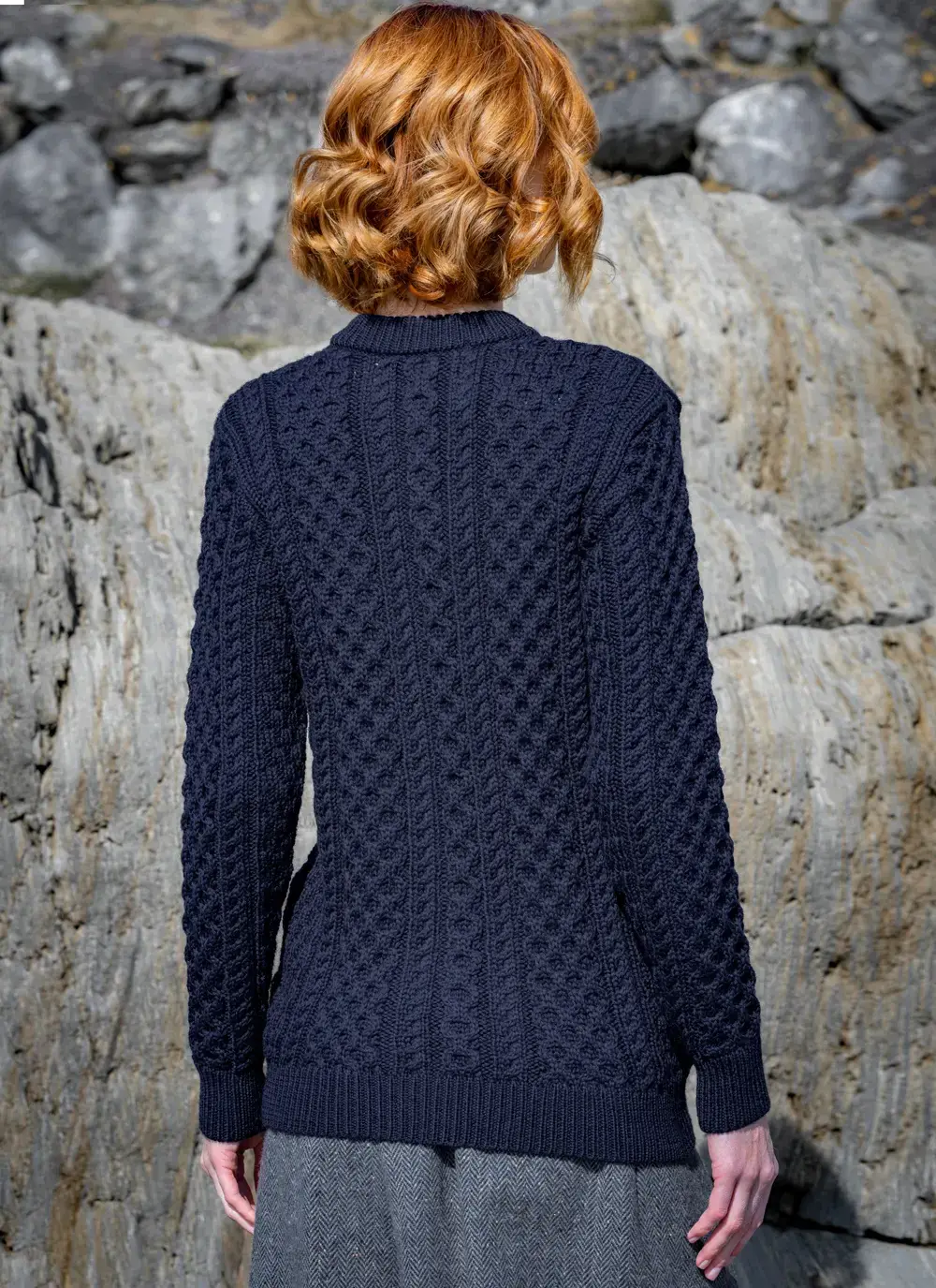 red head model standing on rock looking away backside in dark navy mary lumber aran cardigan