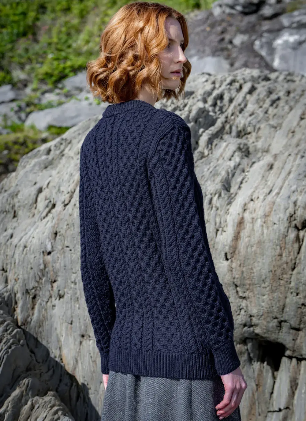 red head model standing on rock looking away backside in dark navy mary lumber aran cardigan