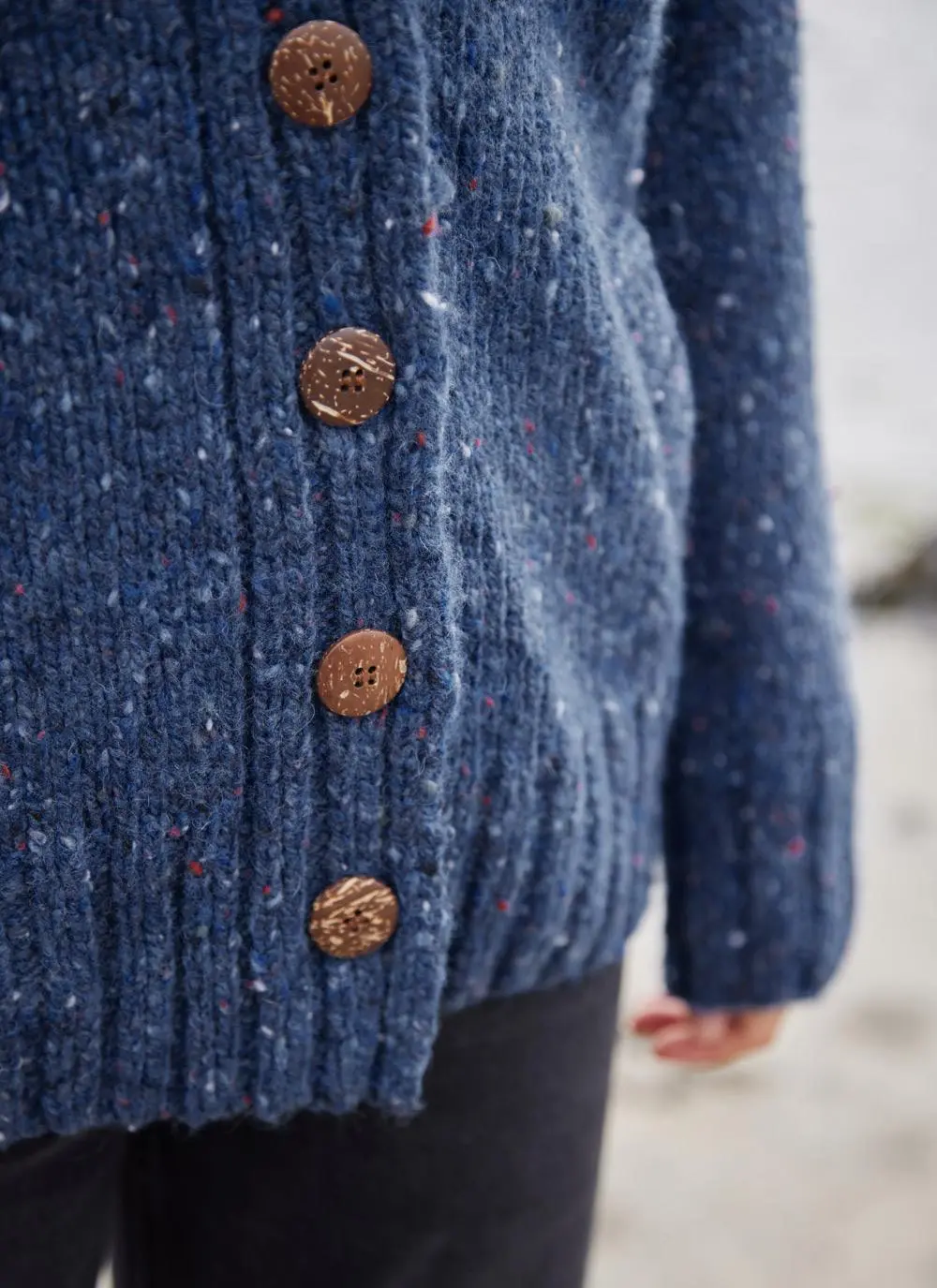 A blue wool cardigan is shown in a close up photograph showing off the buttons and stitching of the cardigan. 