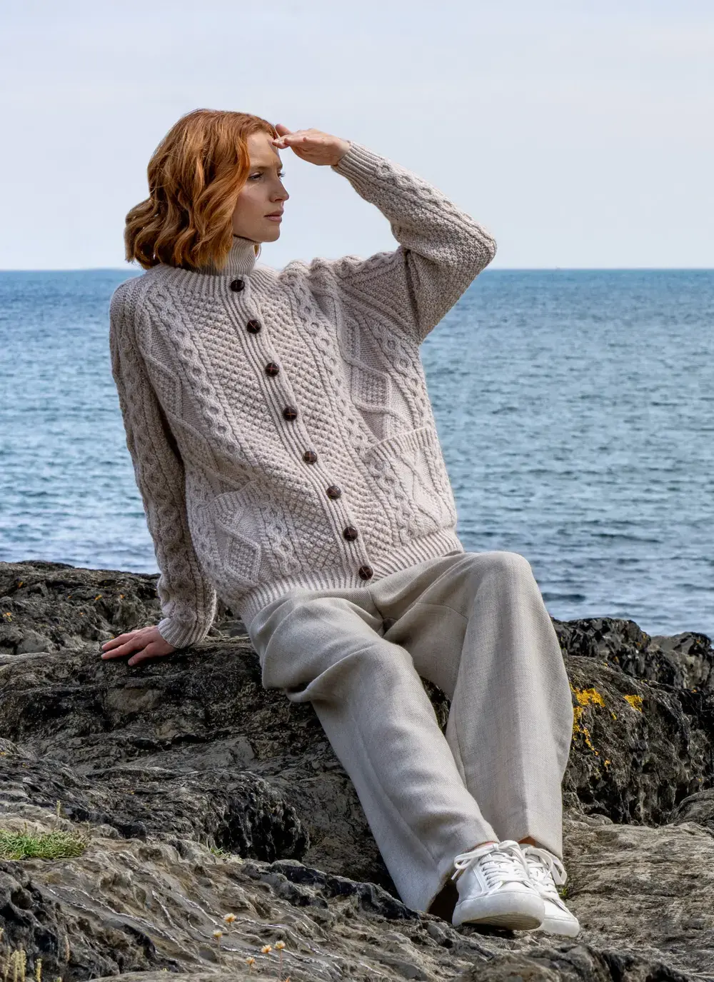 Red head model wearing a traditional hand knit aran lumber in Oatmeal looking out to sea