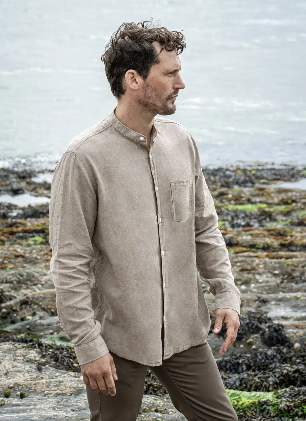 Model wearing Donal Cotton Linen Grandfather Shirt front-on, standing against a rugged stone backdrop in outdoor natural light.