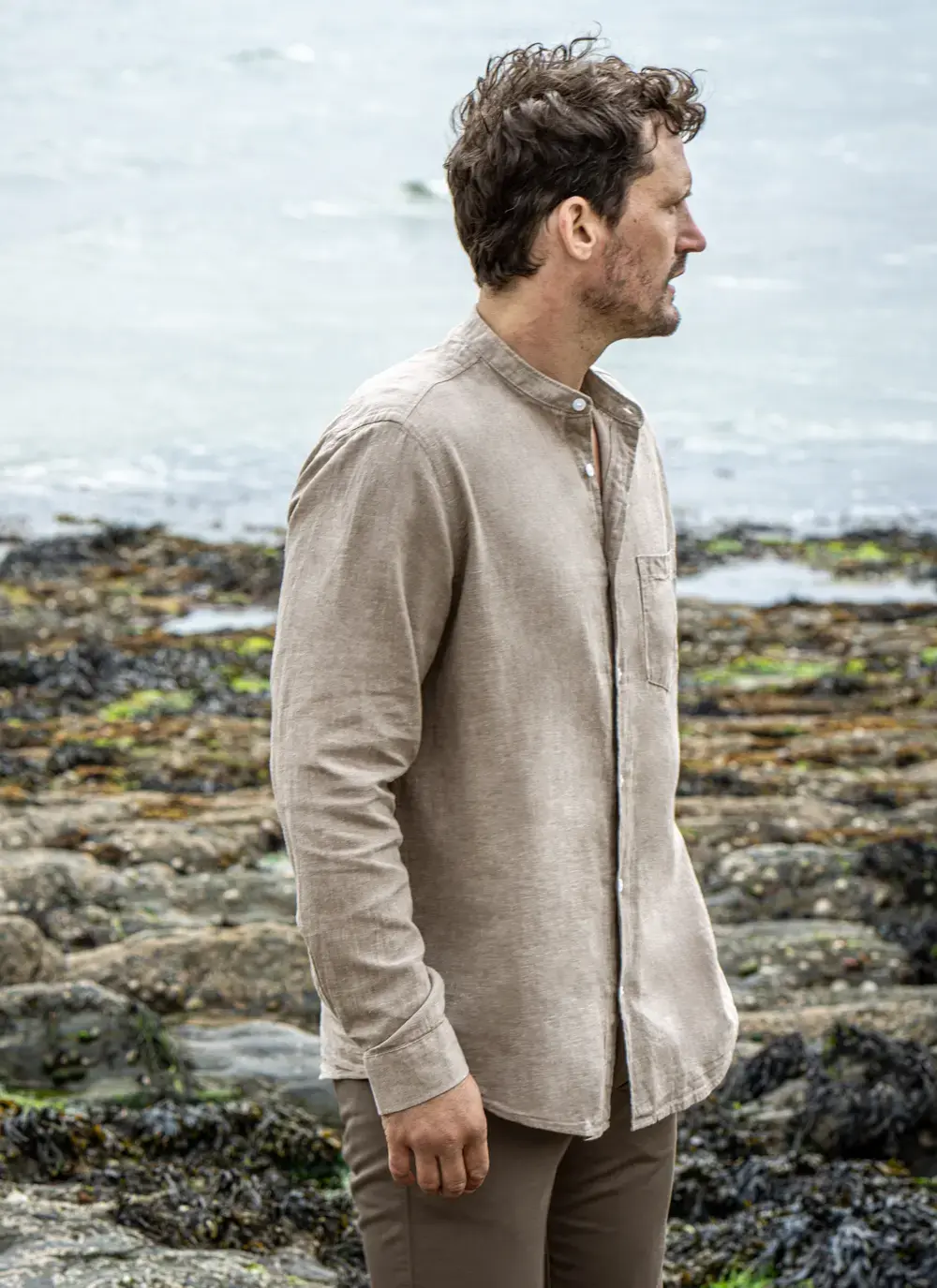 Model wearing Donal Cotton Linen Grandfather Shirt front-on, standing against a rugged stone backdrop in outdoor natural light.