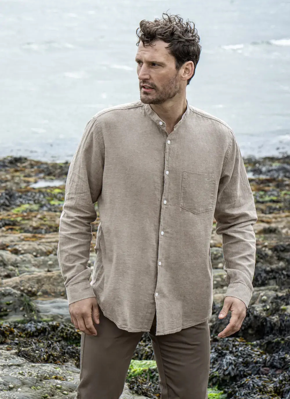 Model wearing Donal Cotton Linen Grandfather Shirt front-on, standing against a rugged stone backdrop in outdoor natural light.