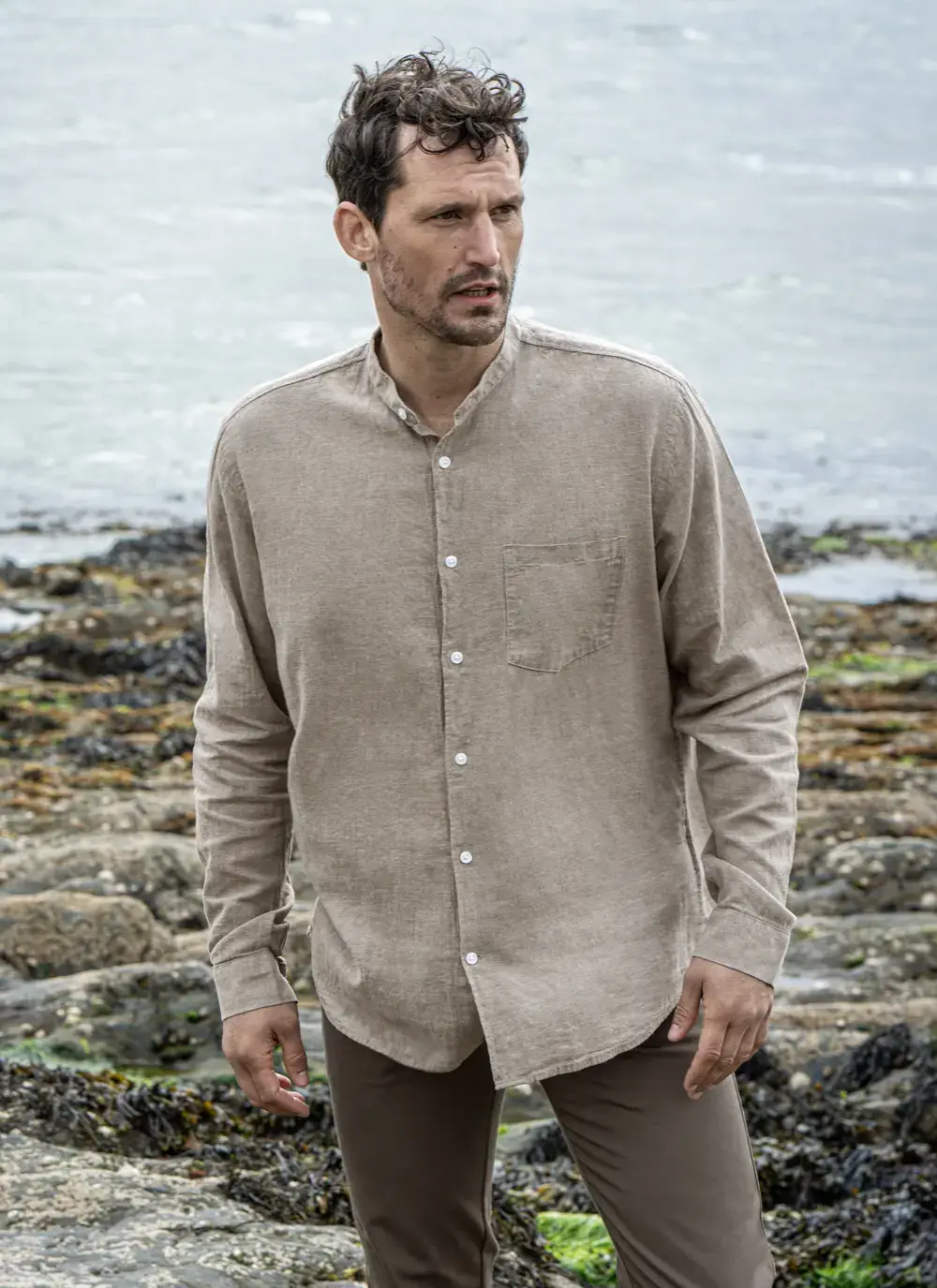 Model wearing Donal Cotton Linen Grandfather Shirt front-on, standing against a rugged stone backdrop in outdoor natural light.