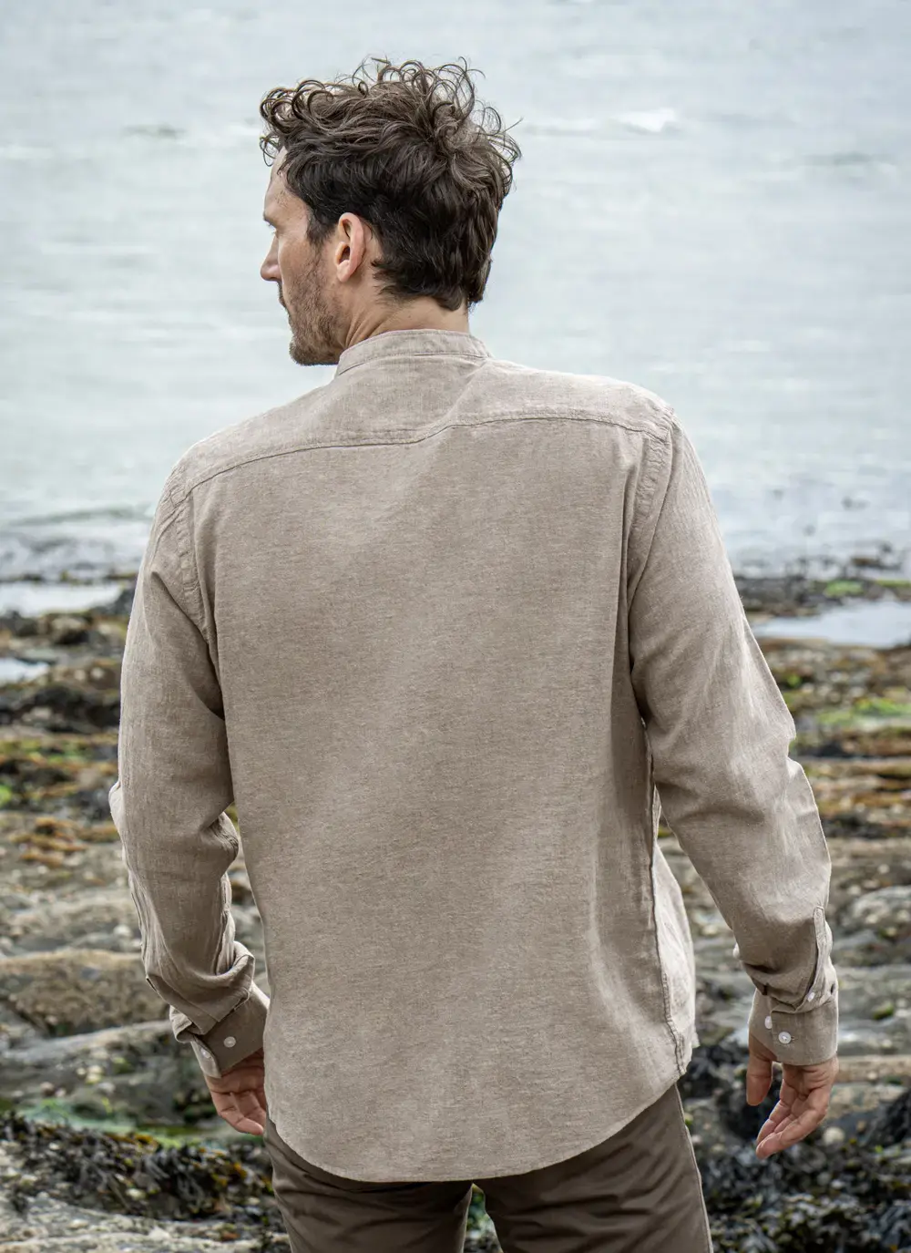 Model wearing Donal Cotton Linen Grandfather Shirt front-on, standing against a rugged stone backdrop in outdoor natural light.