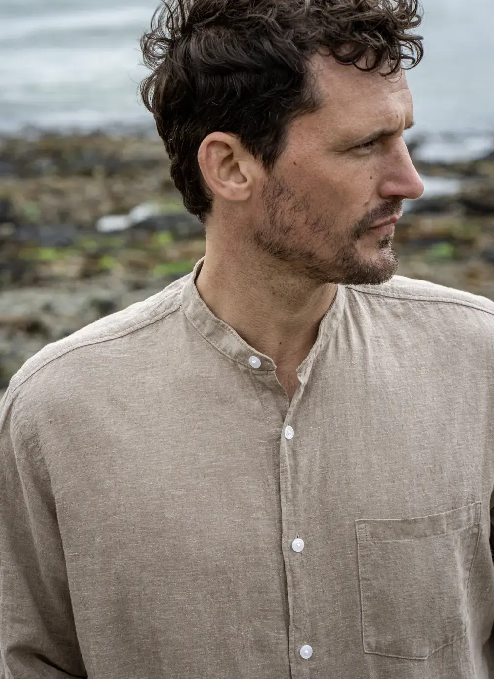 Model wearing Donal Cotton Linen Grandfather Shirt front-on, standing against a rugged stone backdrop in outdoor natural light.