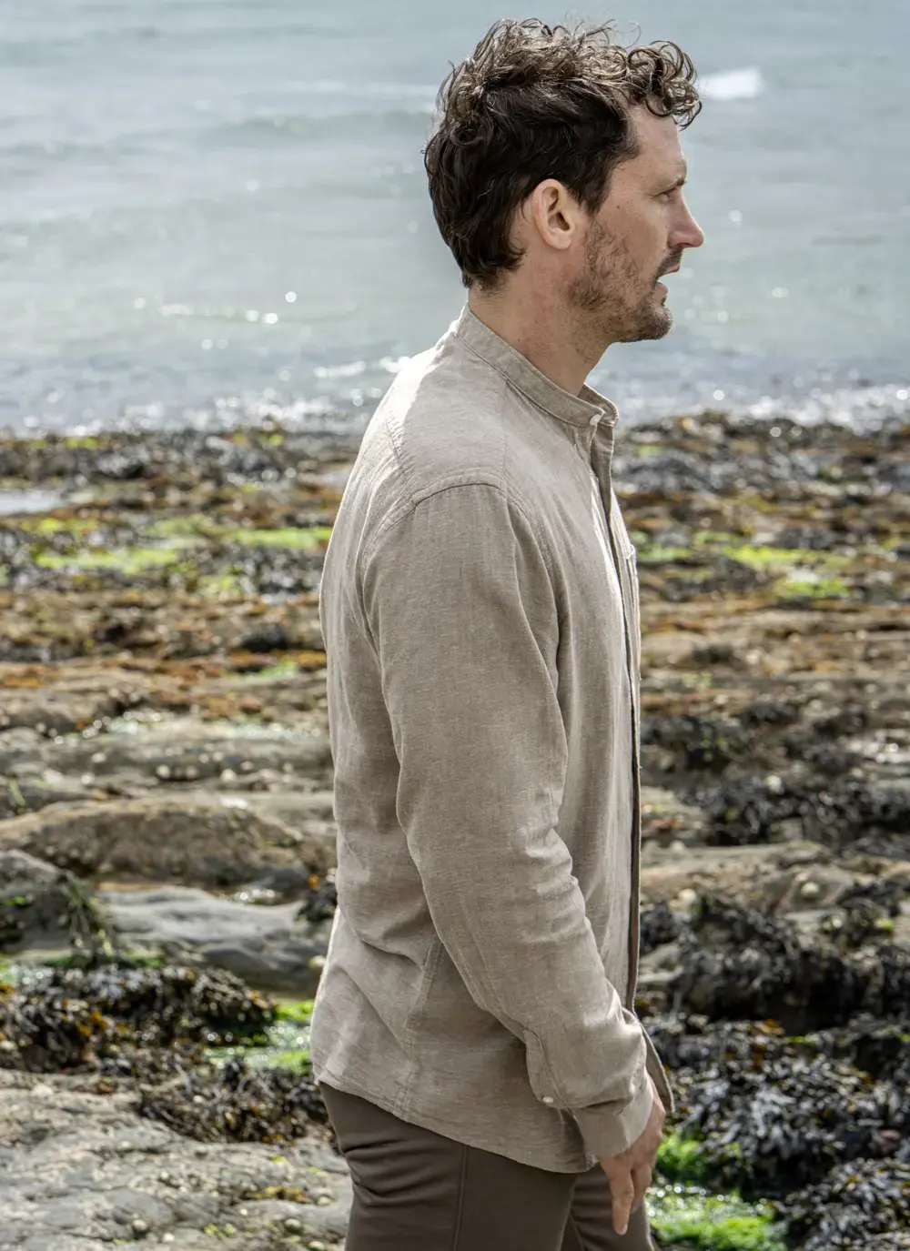 Model wearing Donal Cotton Linen Grandfather Shirt front-on, standing against a rugged stone backdrop in outdoor natural light.