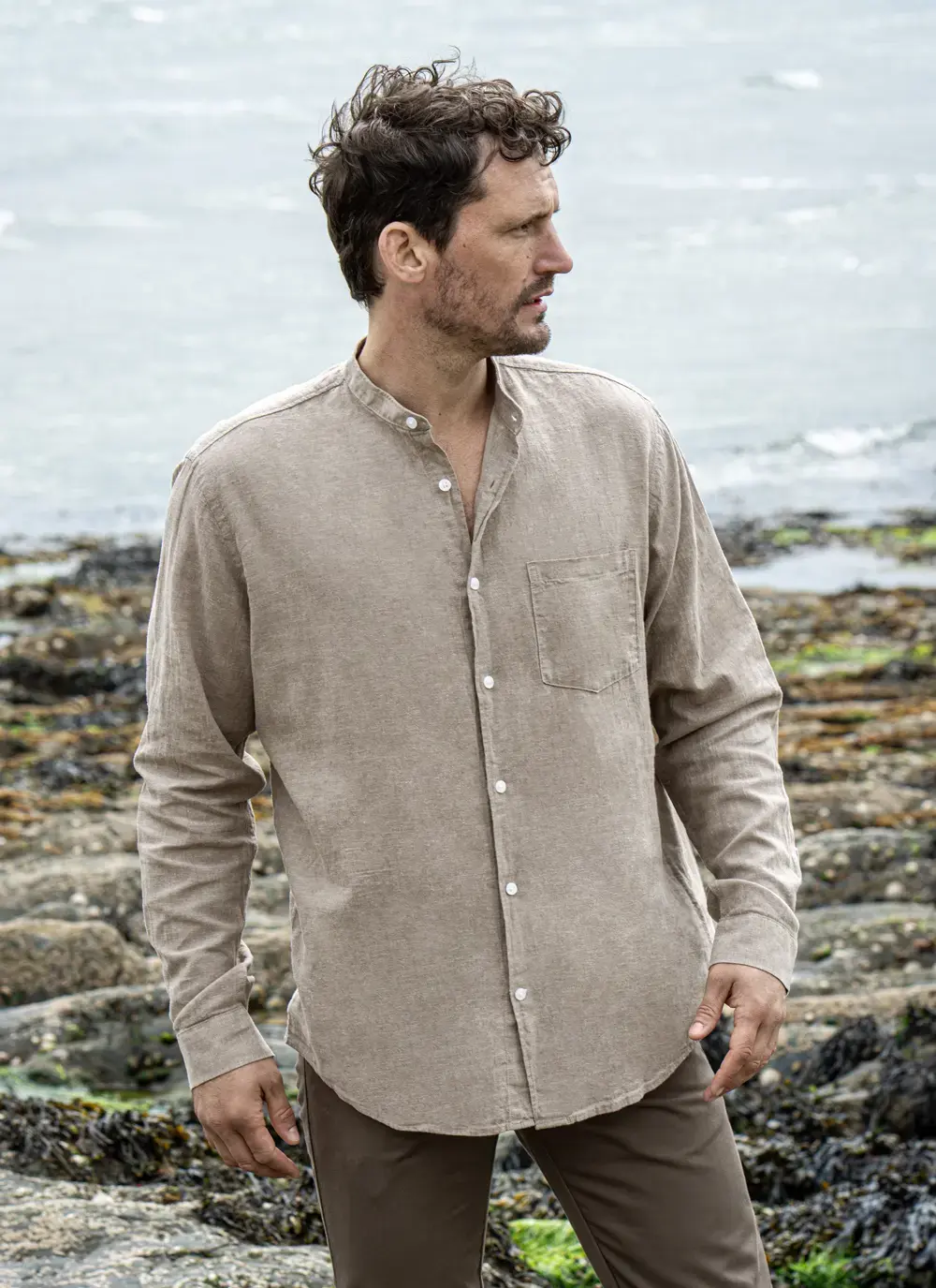 Model wearing Donal Cotton Linen Grandfather Shirt front-on, standing against a rugged stone backdrop in outdoor natural light.