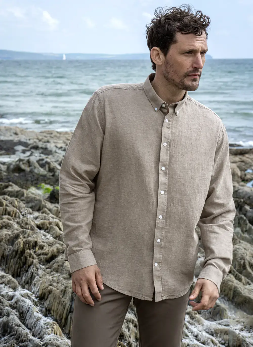Man standing on coastal rocks wearing Finn cotton linen shirt, front angle view