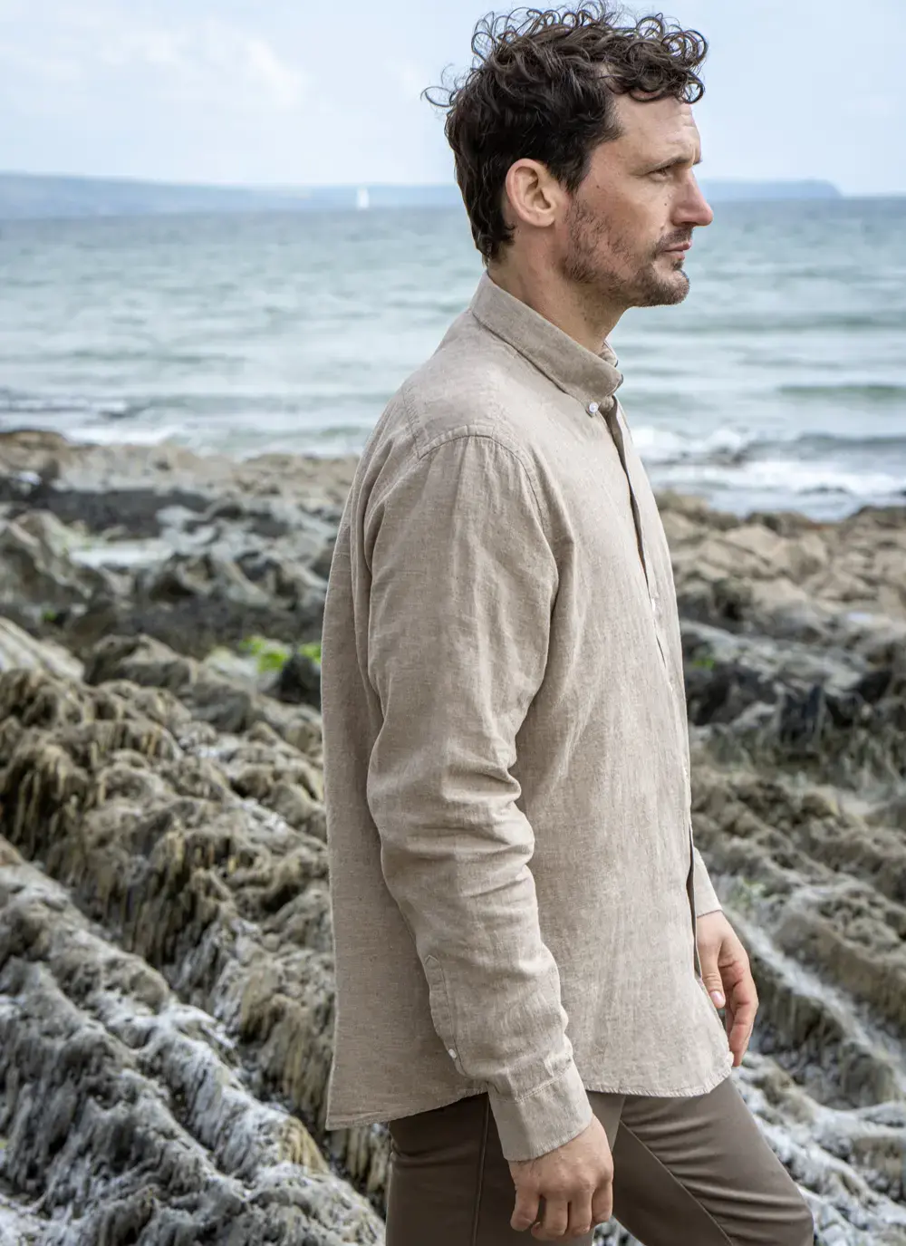Side profile of man wearing Finn cotton linen shirt, mid-shot, by the sea