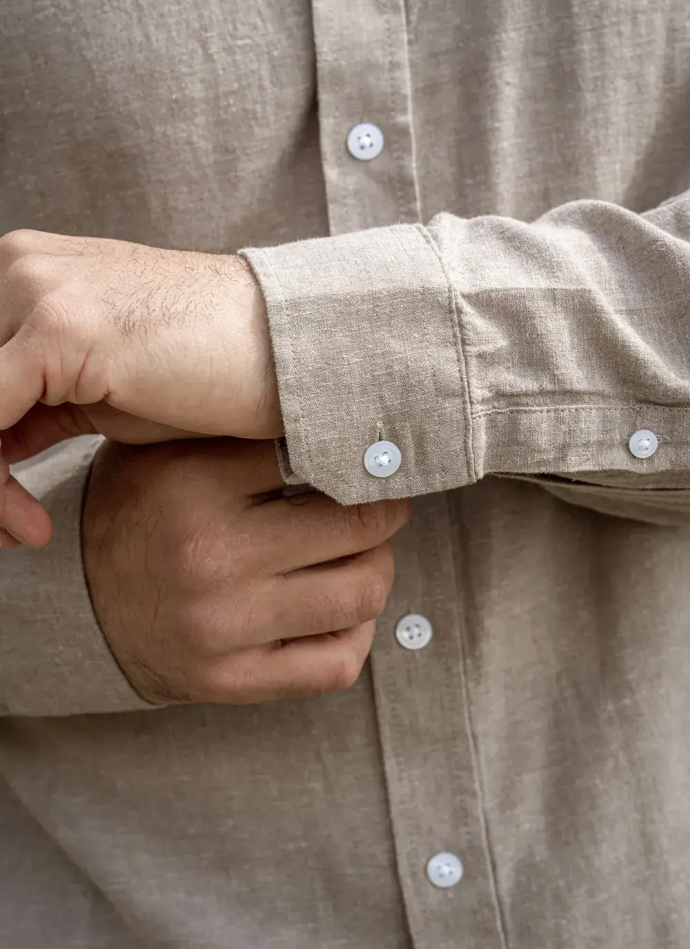 Close-up of man’s hand adjusting cuff of Finn cotton linen shirt, button detail shown