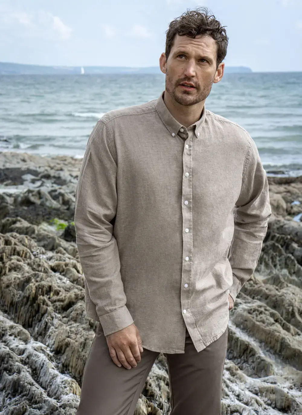 Man standing on coastal rocks wearing Finn cotton linen shirt, front angle view