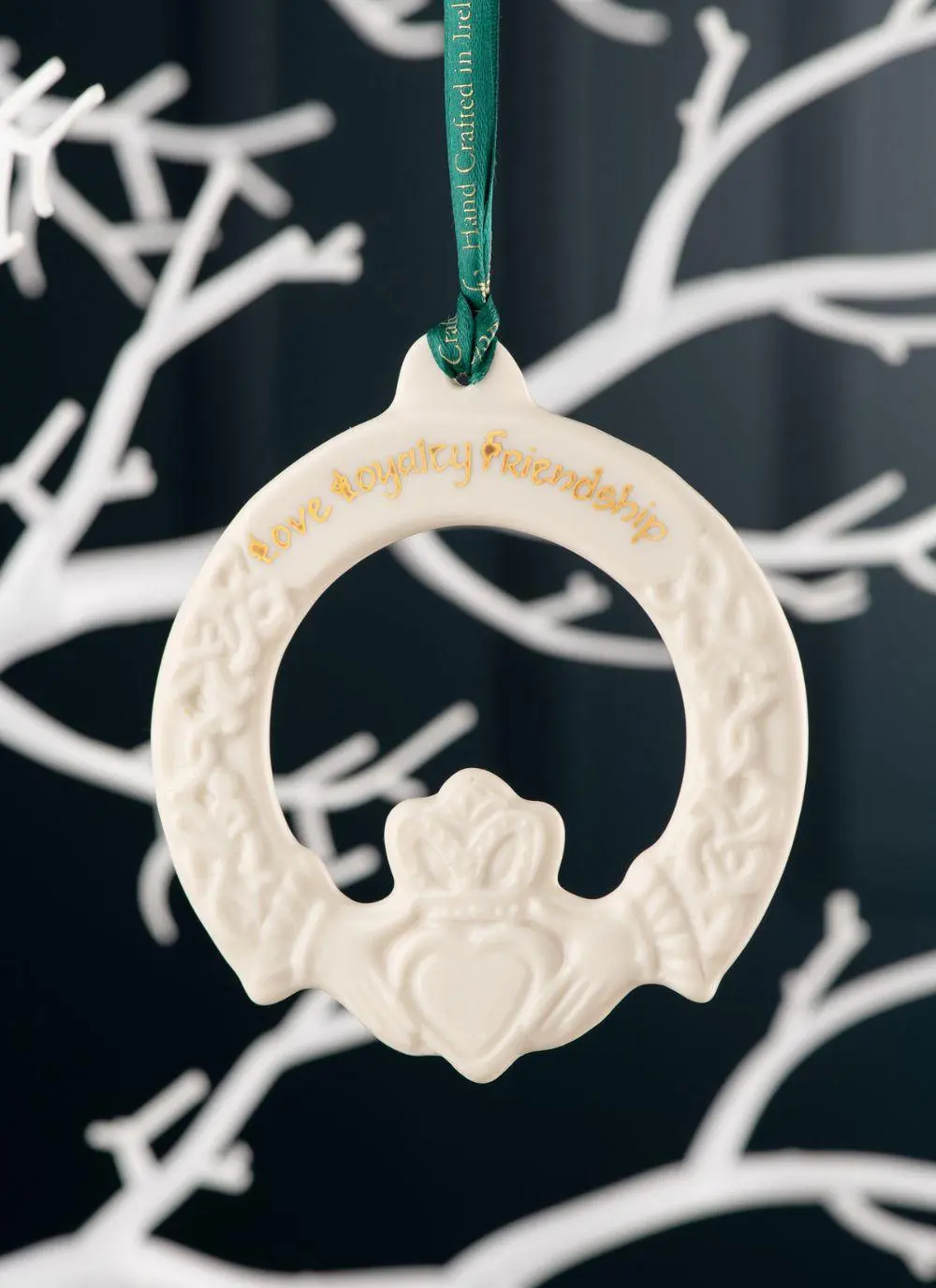 Claddagh Friendship Ornament with inscription love, loyalty and friendship in gold hanging from a green ribbon, on a dark blue background