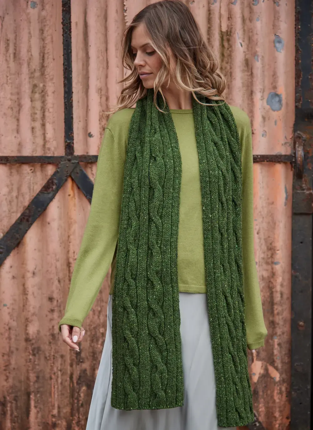 Woman wearing a shamrock green Fisherman Donegal fleck cable knit scarf over a light green sweater.