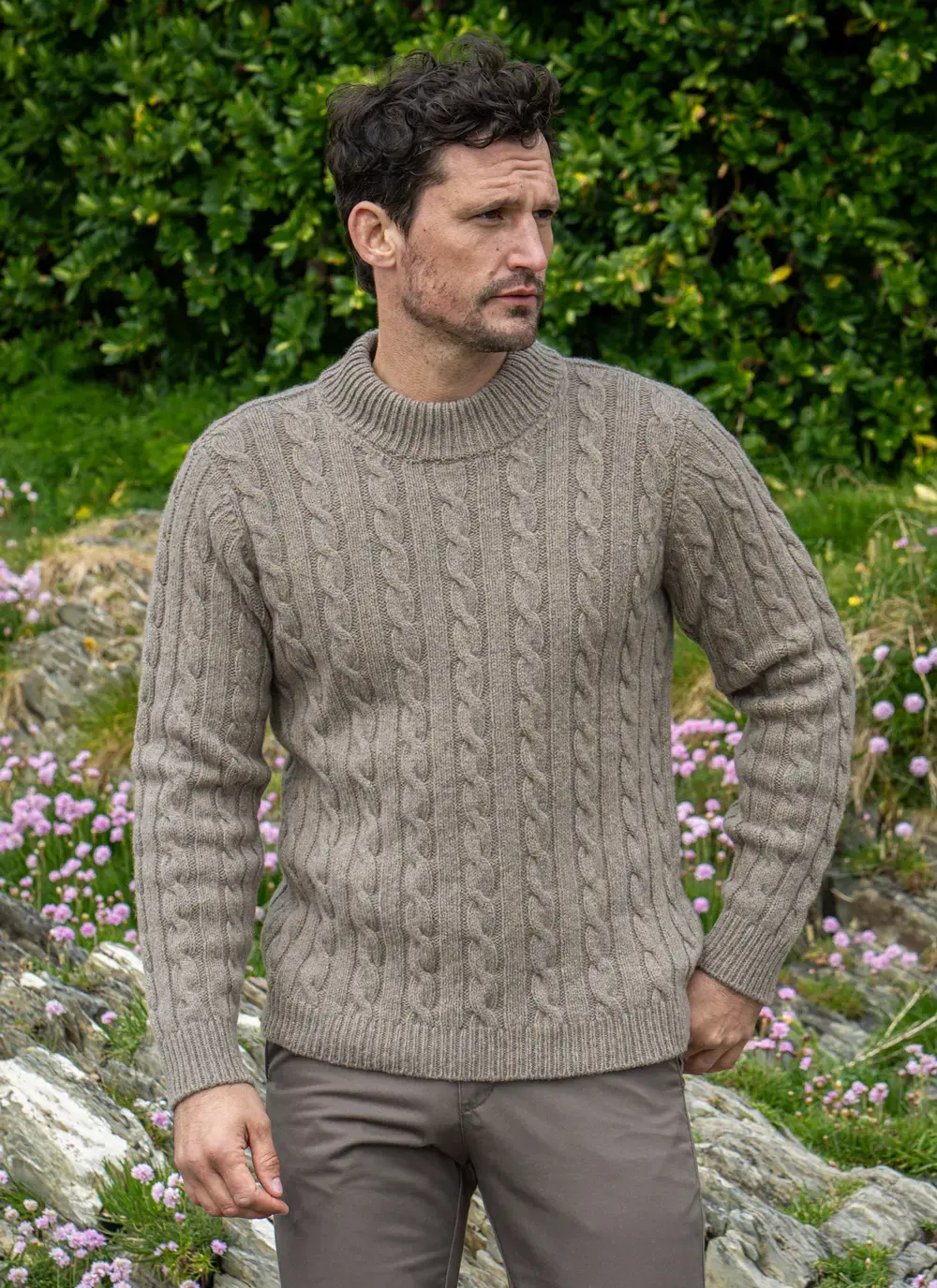 Close-up of Fisherman Cable Knit Sweater in Clay, featuring textured cable design and ribbed hem, styled with taupe trousers.