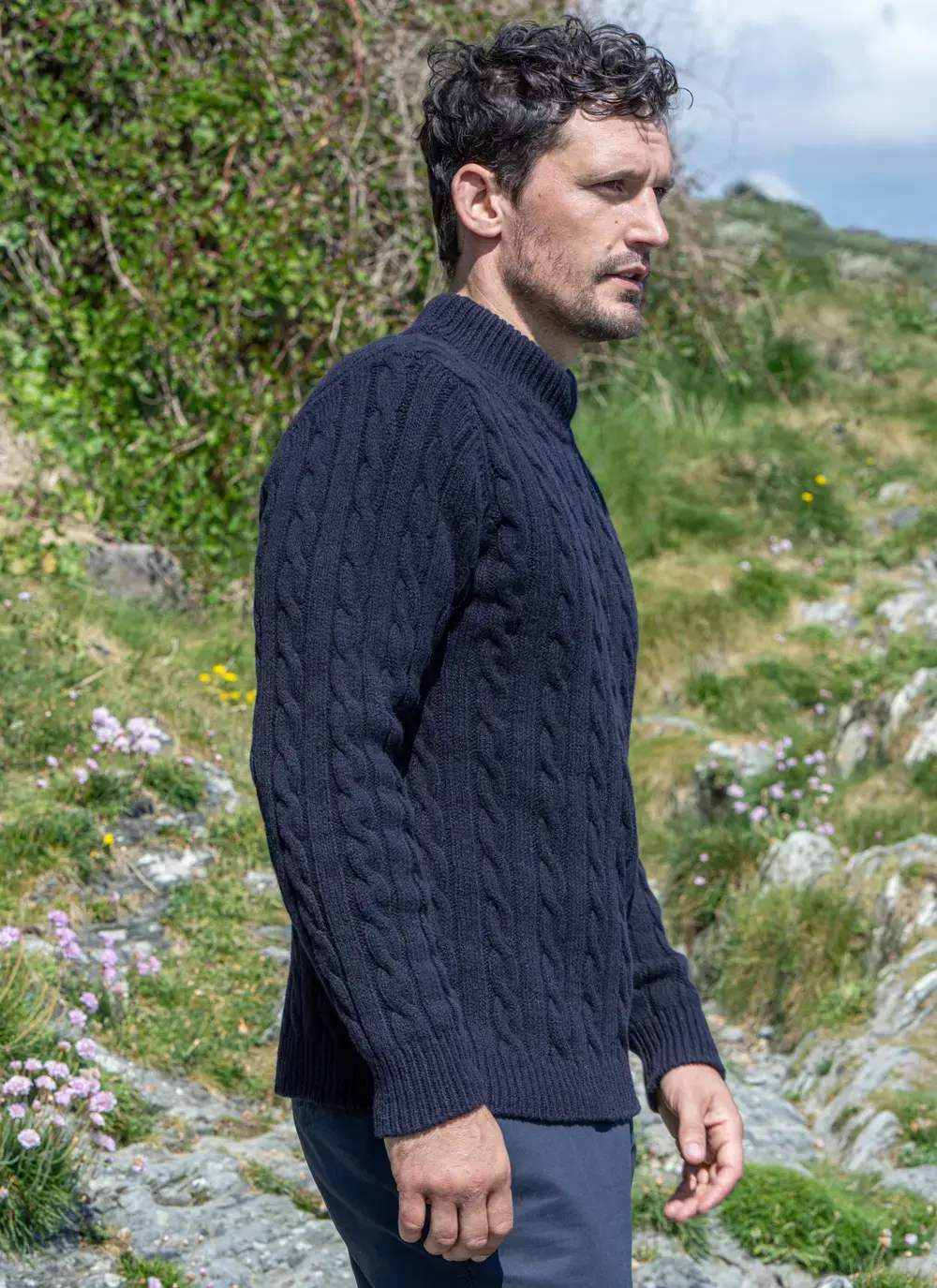 Profile view of man in navy cashmere wool sweater, with hand in pocket and outdoor floral background.