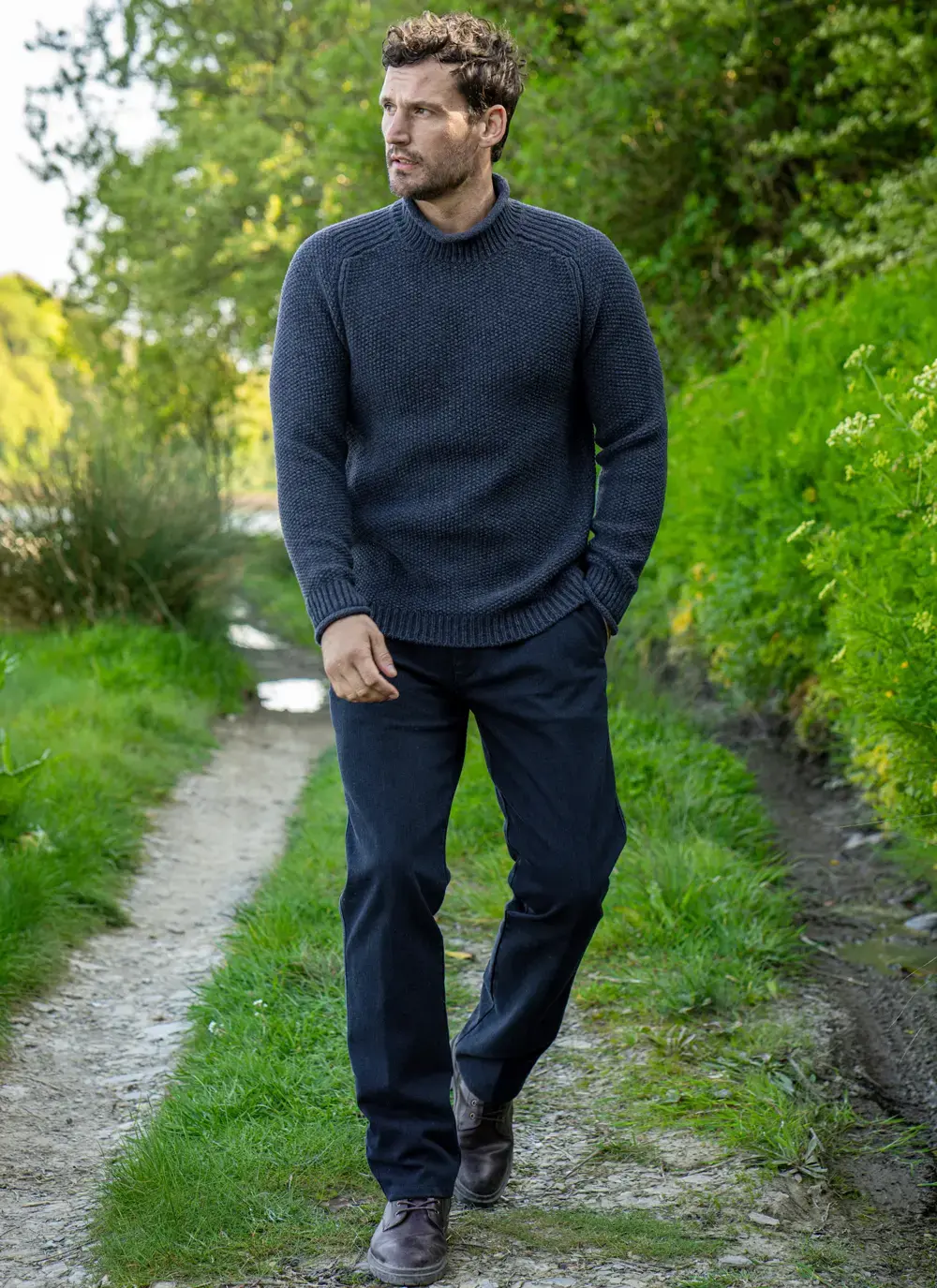 Man wearing Fisherman Cashmere Seed Stitch Roll Neck Sweater in dark indigo walking on a path
