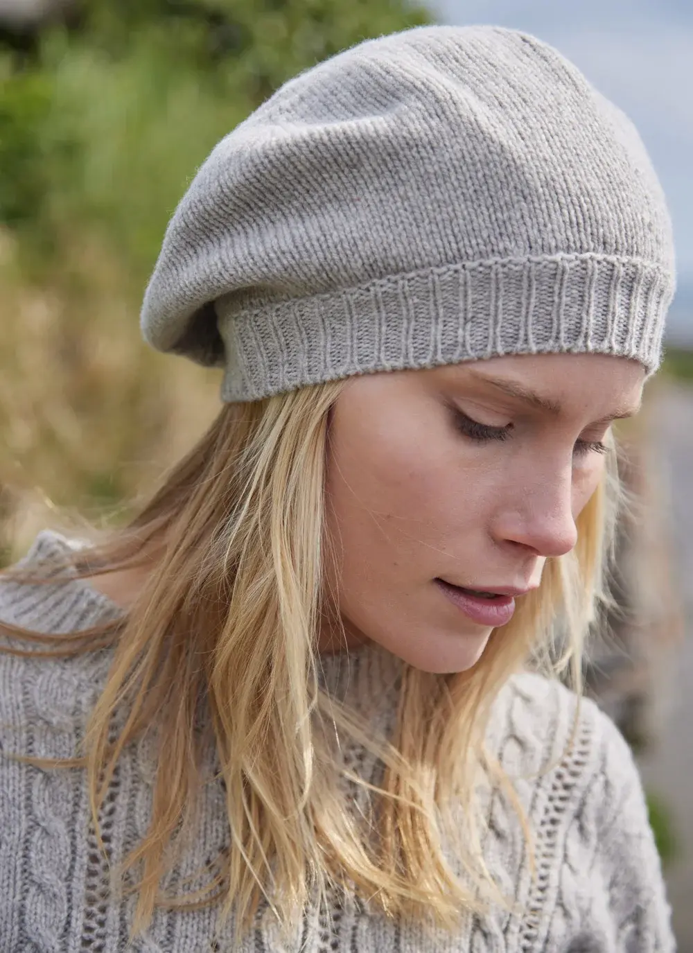 Blonde woman wearing beige woolen beret with grass in background