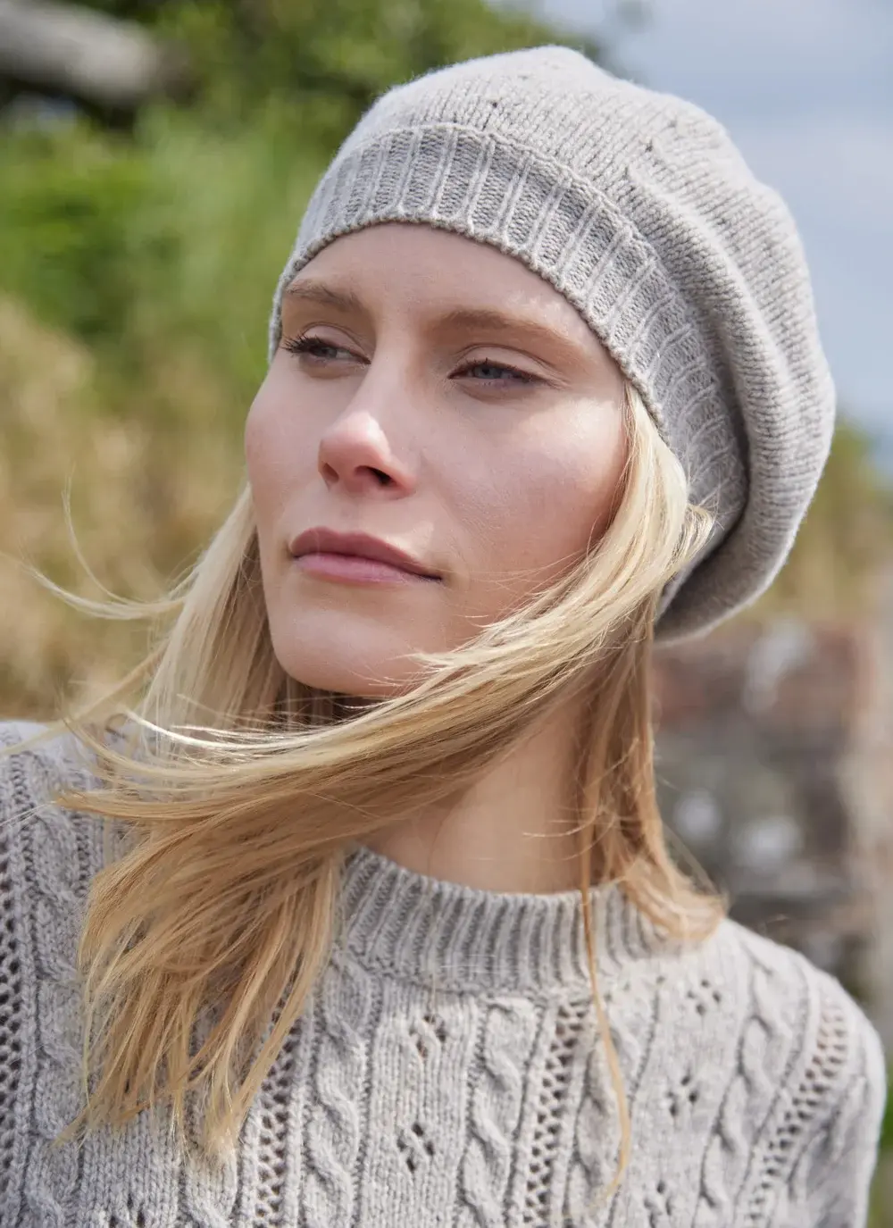Blonde woman wearing beige woolen beret with grass in background