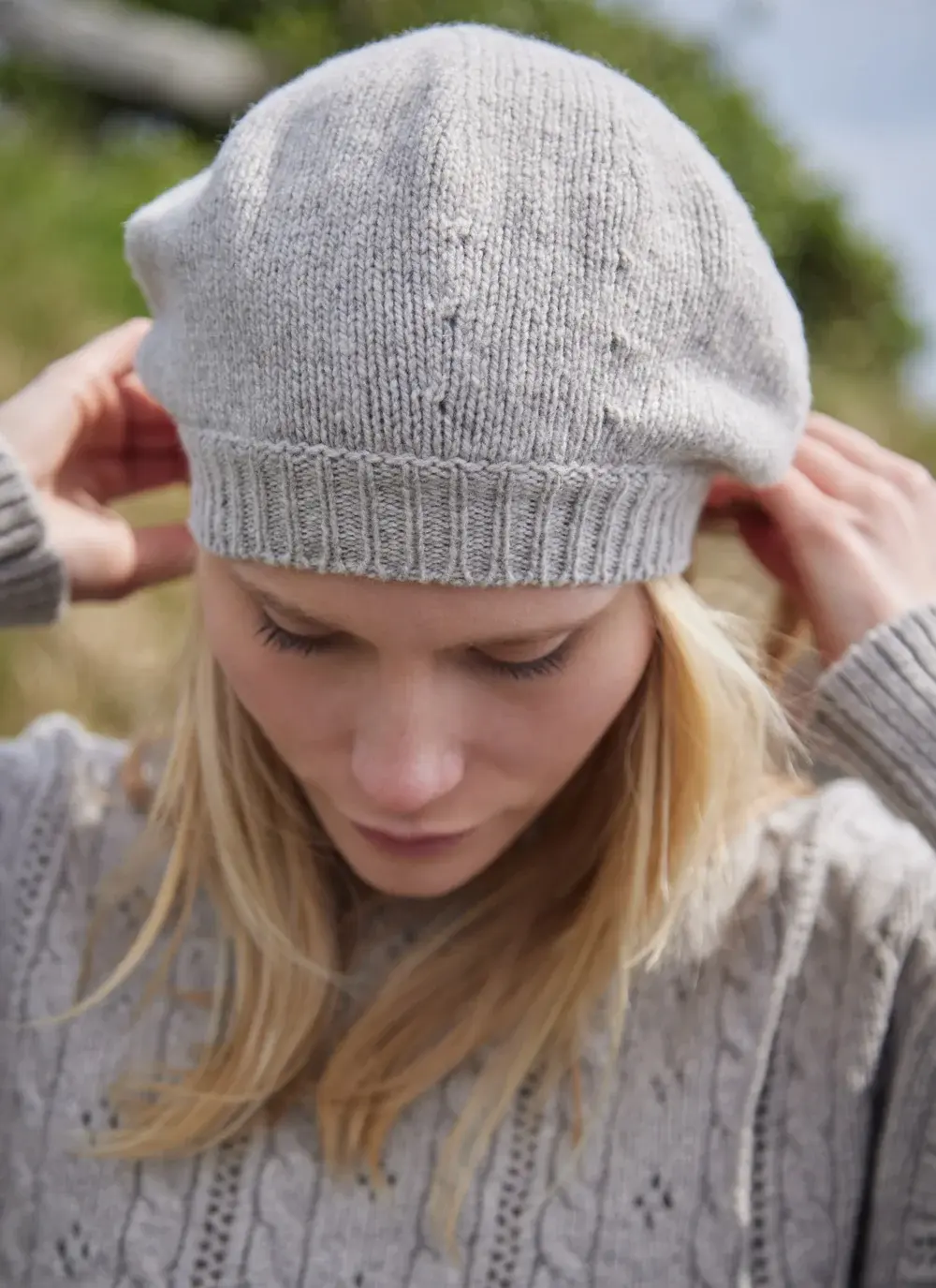 Blonde woman wearing beige woolen beret with grass in background