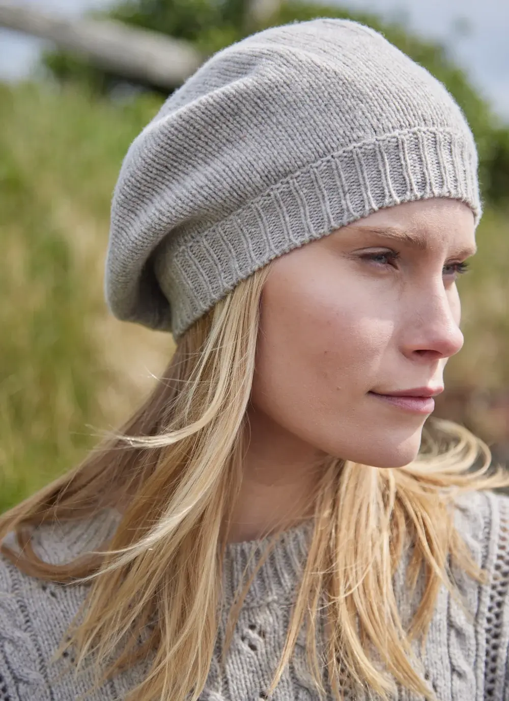Blonde woman wearing beige woolen beret with grass in background