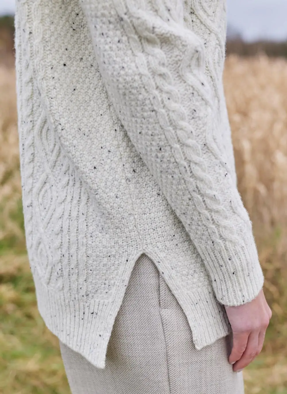 Close up shot of woman in field wearing ecru colored Aran turtle neck sweater