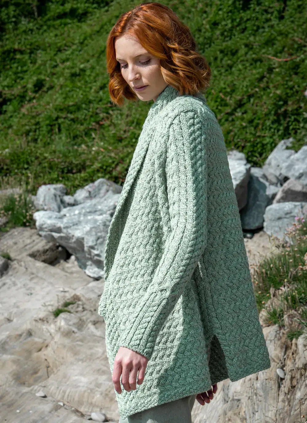Red headed model side profile in front of greenery in sage green glenross aran waterfall cardigan