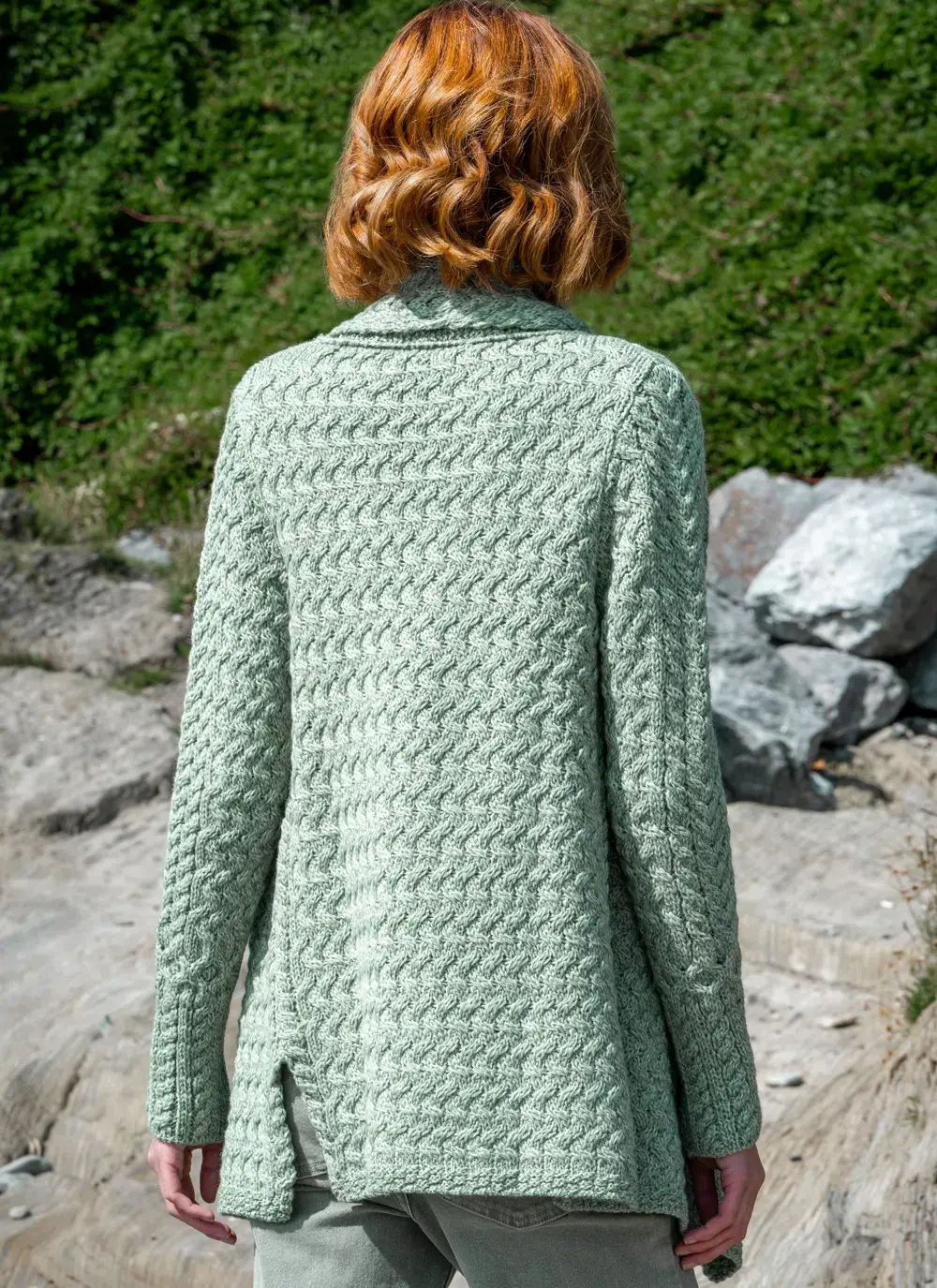 Red headed model facing greenery background in sage green glenross aran waterfall cardigan