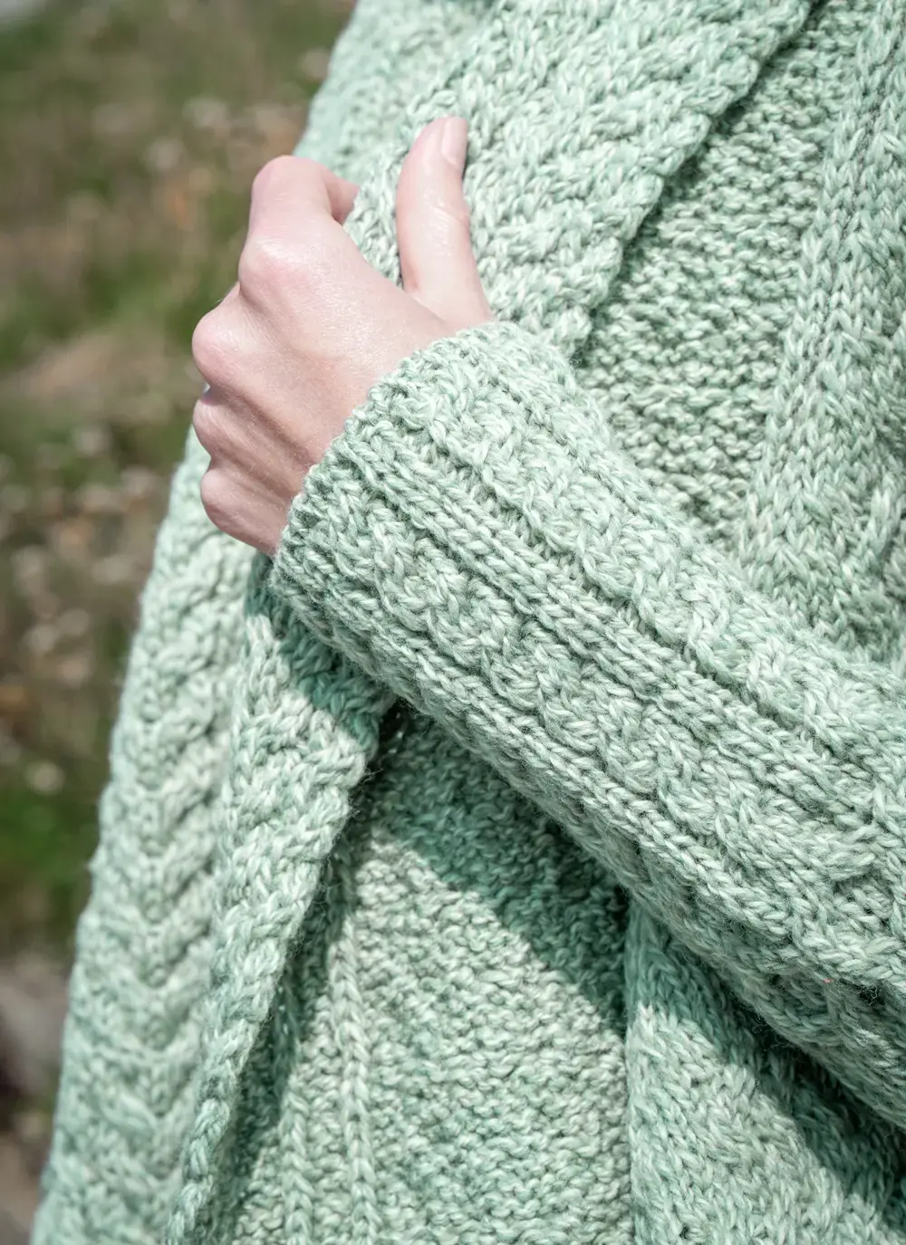 Close up shot of model sleeve detail in front of rocky background glenross aran waterfall cardigan holding collar