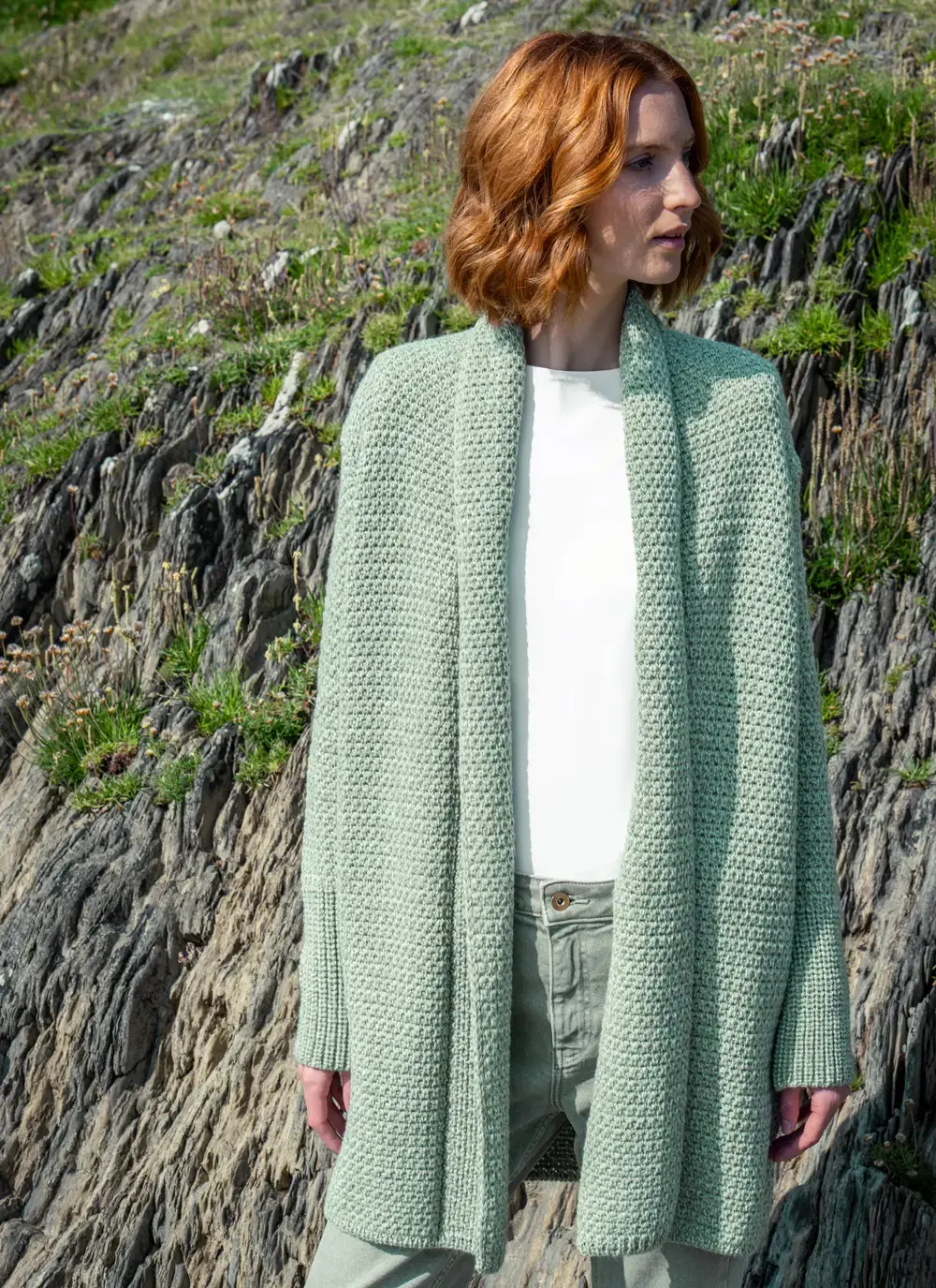 Red headed model standing in rocky wearing a sage green knitted kilcoole textured coatigan