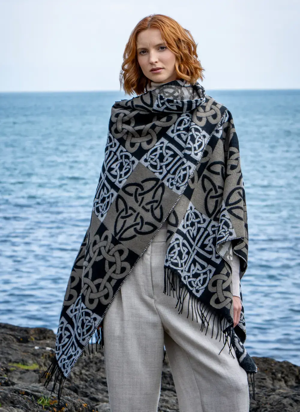 Red head model standing in front of water in black celtic knot shawl draped over shoulder